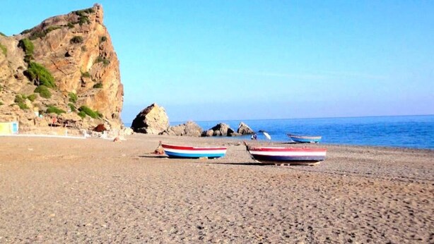 A rocky beach with boats and a cliff.