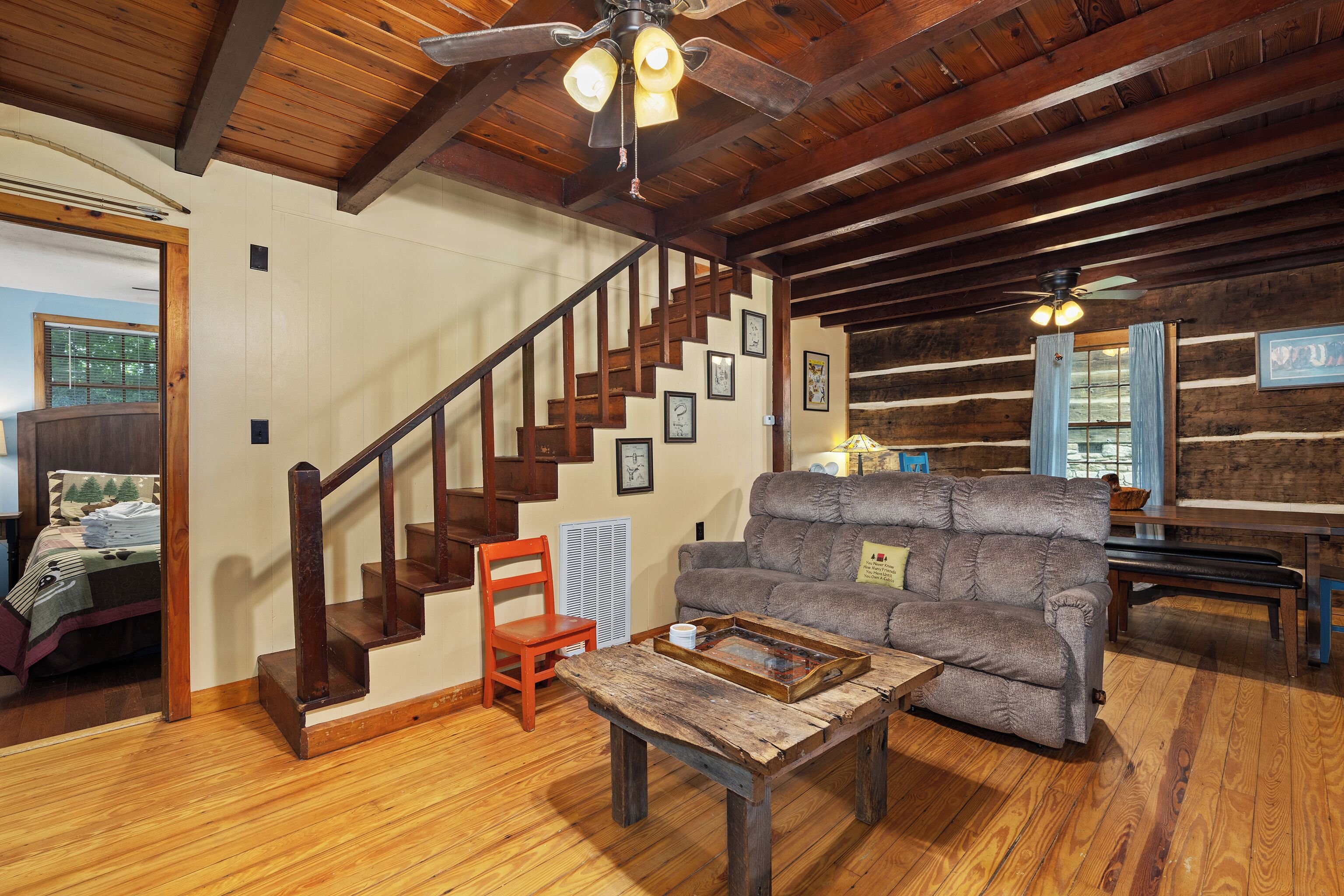 A rustic cabin interior with a wooden staircase, a sofa, and a dining table.