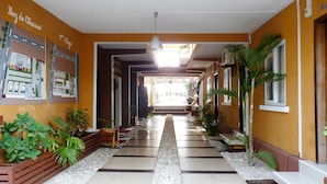 A hotel corridor with tiled flooring, potted plants, and a view into the lobby area. - La Fourmi Hôtel (Nosy Be)