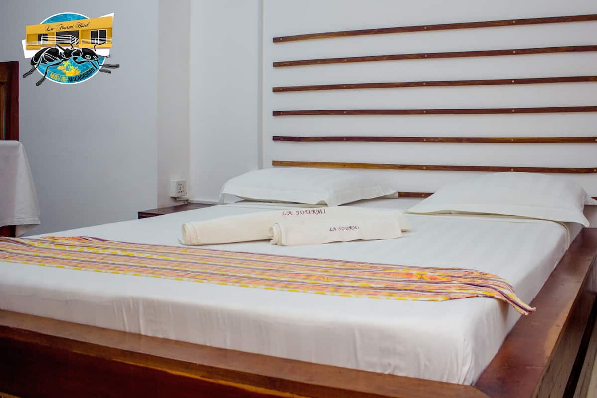 A hotel room with a bed, wooden headboard, white linens, and towels with "LA TOURMI" branding.