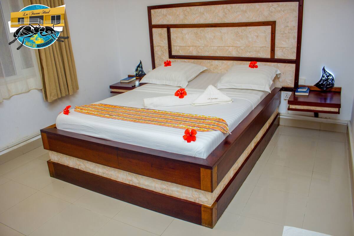 A large bed with a wooden frame, white bedding, and red flowers. There are two bedside tables with books and a decorative item.