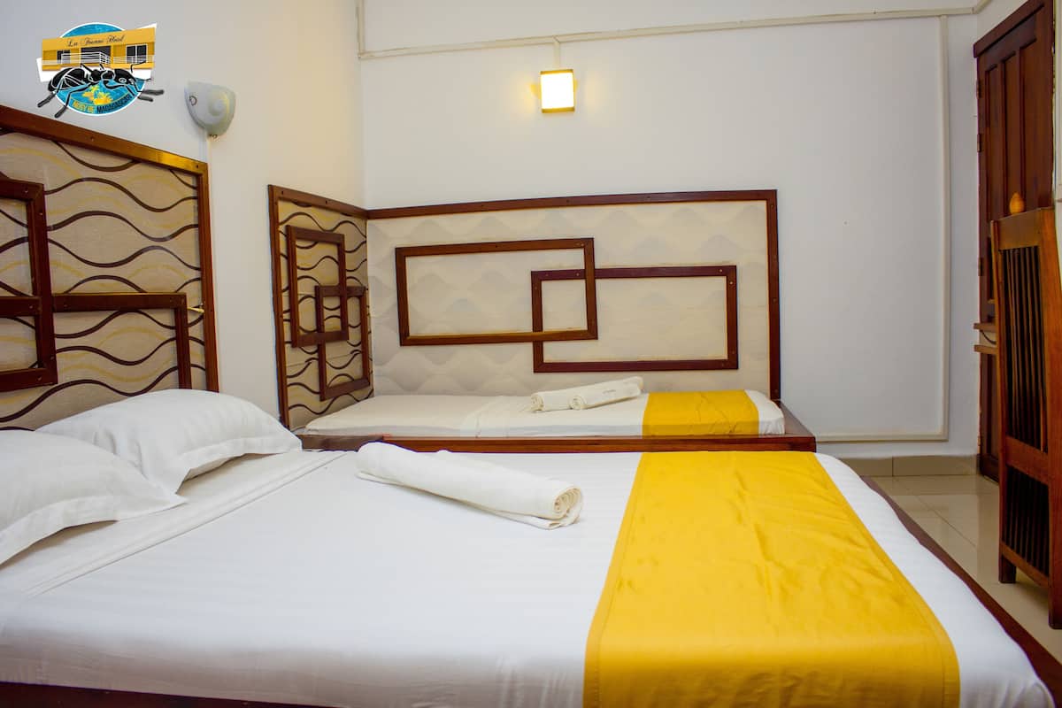 A hotel room with two beds, one with a yellow bedspread and the other with a white bedspread.