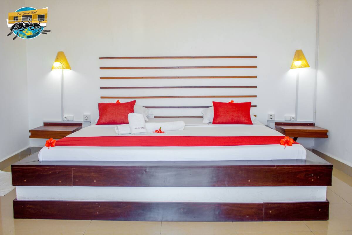A large bed with a wooden headboard, red and white bedding, and two bedside lamps.