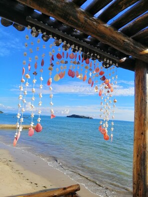A beach scene with a wooden structure and hanging shells. - La Fourmi Hôtel (Nosy Be)