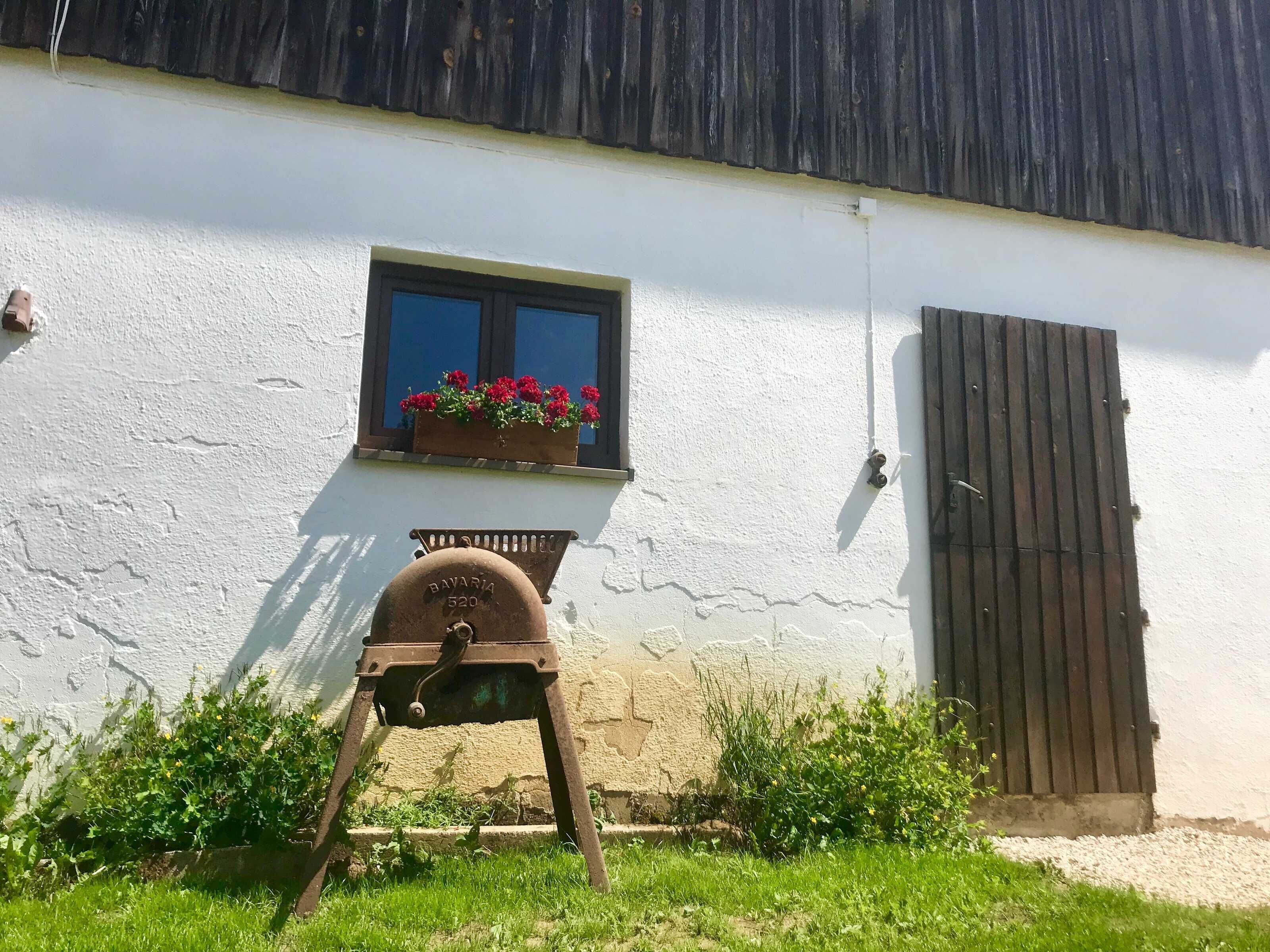 A white building with a window, a wooden door, and a metal barrel with the number 520.
