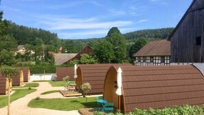 Un paysage rural avec des bâtiments traditionnels en bois, un ciel dégagé et une colline boisée en arrière-plan.