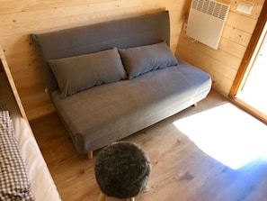 Ein Holzinnenraum mit einer Couch, einem kleinen Hocker und einem Wandlüfter.