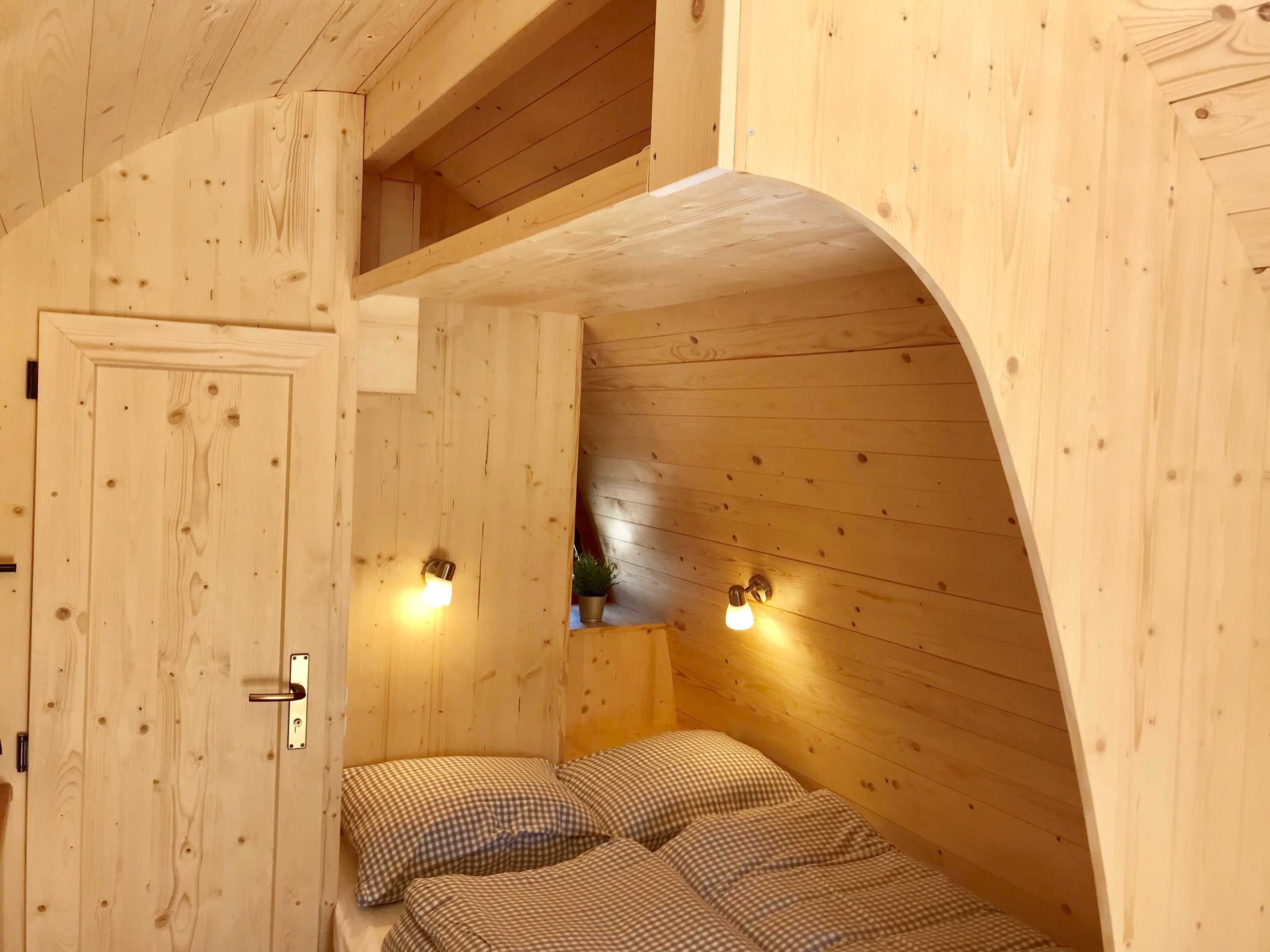 A wooden room with a bed, two wall-mounted lights, and a door.