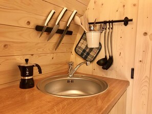 Eine Küche mit Holztischplatte, einer Edelstahl-Spüle, einer Kaffeemaschine und Geschirr an einem Gestell.