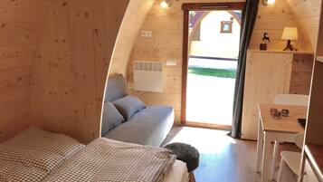 Une pièce chaleureuse, aménagée dans une cabane en bois, avec un lit, un petit bureau et une fenêtre.