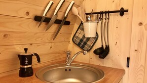 Eine Küche mit Holztischplatte, einer Edelstahl-Spüle, einer Kaffeemaschine und Geschirr an einem Gestell.