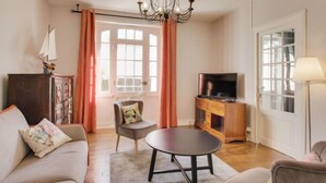 A living room with a sofa, armchair, coffee table, TV, and a chandelier.