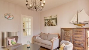 A cozy living room with a round table, a sofa, a chair, a wooden cabinet, a chandelier, a clock, and a sailboat model.