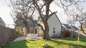 A house with a stone facade, a large tree in the front yard, and a patio with white chairs.