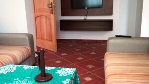 Une chambre d’hôtel avec deux lits, un téléviseur fixé au mur, une porte en bois et un sol carrelé.