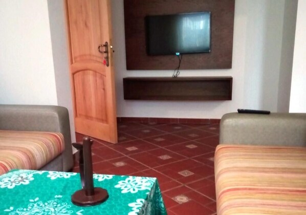 A hotel room with two beds, a TV mounted on the wall, a wooden door, and a tiled floor.