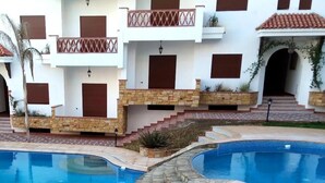 Un espace piscine comprenant deux piscines, des marches en pierre et un bâtiment doté de balcons et de fenêtres.