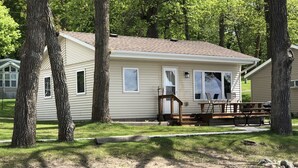 A single-story mobile home with a covered patio area, surrounded by trees. - Lake Miltona, MN Weekly Rental Cabin is located right on the beach. (Miltona)