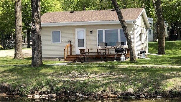 A single-story house with a deck, a picnic table, and a small porch area. - Lake Miltona, MN Weekly Rental Cabin is located right on the beach. (Miltona)