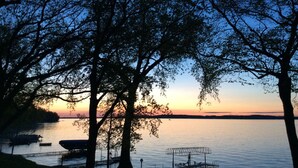 A serene lakeside view with trees framing the sunset. Boats are docked along the shore. - Lake Miltona, MN Weekly Rental Cabin is located right on the beach. (Miltona)