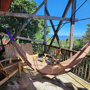 A wooden deck with a hammock, wooden chairs, and a view of the landscape.