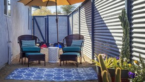 Une terrasse avec deux fauteuils en osier, un tapis Ă motifs et un cactus en pot.