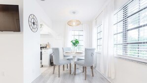 A bright dining area with a round table, four grey chairs, a hanging light fixture, and a large window with blinds. - Beautiful Waterfront Condo on Canal with Pool & Walk to Beach! Boat Watch! 1b/1b (Pompano Beach)