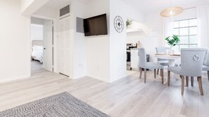 A modern living room with a dining area, a TV mounted on the wall, and a kitchen in the background. - Beautiful Waterfront Condo on Canal with Pool & Walk to Beach! Boat Watch! 1b/1b (Pompano Beach)