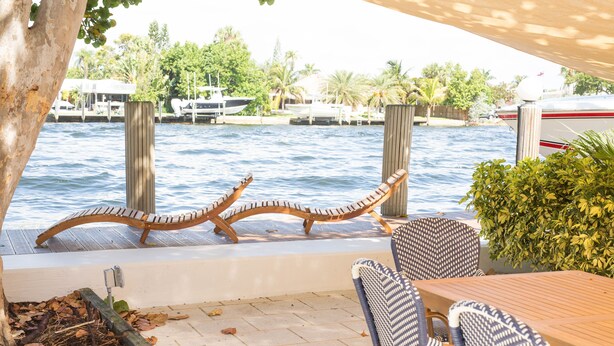 A patio with a wooden table and chairs, overlooking a marina with boats. - Beautiful Waterfront Condo on Canal with Pool & Walk to Beach! Boat Watch! 1b/1b (Pompano Beach)