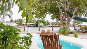 A pool area with wooden lounge chairs, a tree, and a view of the marina with boats. - Beautiful Waterfront Condo on Canal with Pool & Walk to Beach! Boat Watch! 1b/1b (Pompano Beach)