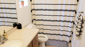 A bathroom with a white sink, wooden cabinets, a toilet, and a shower curtain with a black and white pattern.