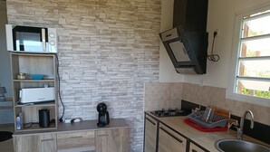 A modern kitchen with a stone backsplash, a microwave, a coffee maker, and a sink. - DOMAINE DECOTTE BUNGALOW in the heart of nature (Sainte-Suzanne)