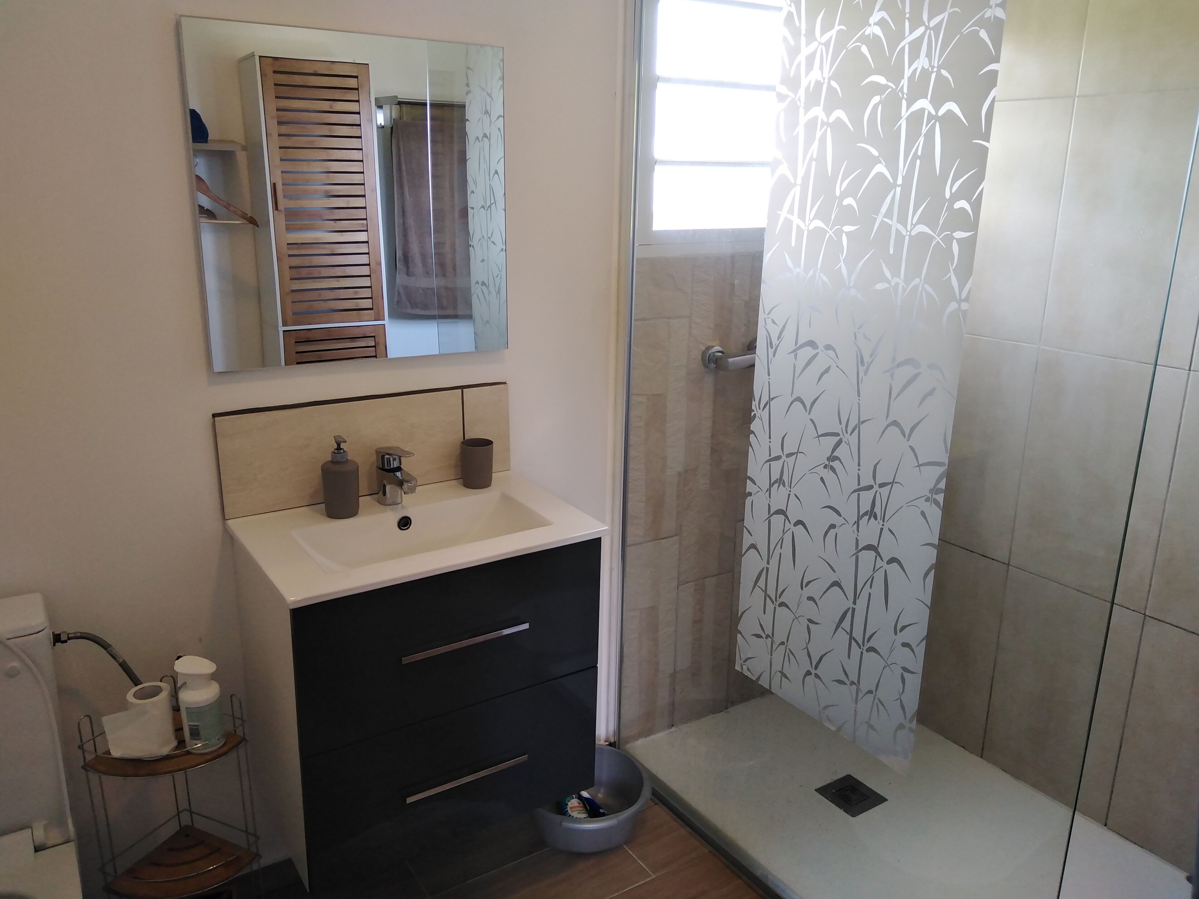 A modern bathroom with a white sink, dark cabinet, and a shower with a bamboo-patterned curtain.
