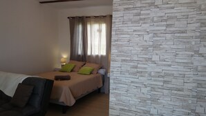 A bedroom with a bed, a nightstand, a lamp, and a stone-textured wall. - DOMAINE DECOTTE BUNGALOW in the heart of nature (Sainte-Suzanne)