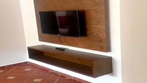 A wall-mounted TV with a wooden panel backdrop and a built-in shelf below. - Residence Alcazaba Oued Laou 4132 (OUED LAW)