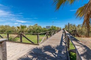 A wooden boardwalk leading through a natural landscape with trees and a clear sky. - Playa Grande - Punta del Moral Beach PPHG67P42 (Punta del Moral)
