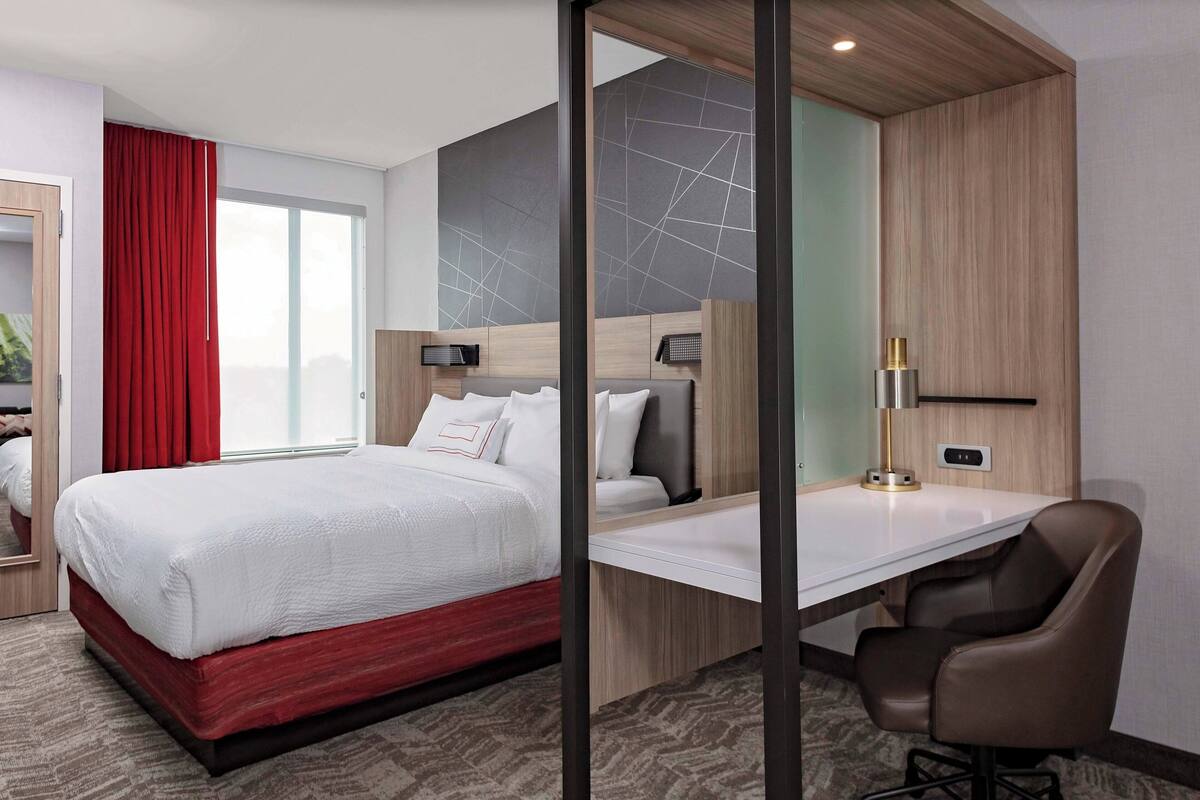 A modern hotel room with a large bed, a desk, and a chair.