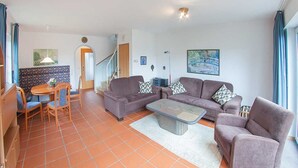 Un salon comprenant un ensemble de canapés, une table basse et une table à manger avec des chaises. Un escalier mène à un autre niveau.