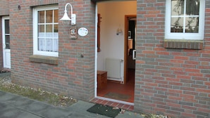 Un bâtiment en briques avec une porte ouverte donnant sur une pièce où se trouvent un radiateur et un meuble en bois.