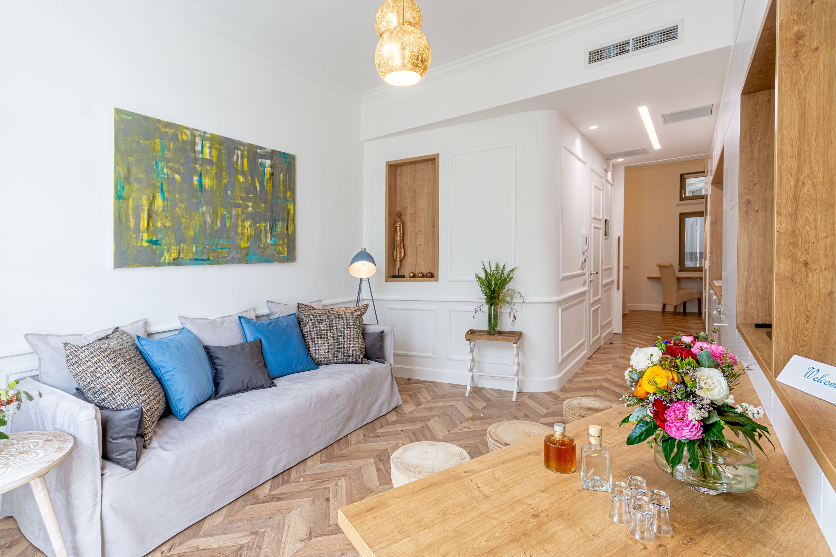 A modern living room with a grey sofa, a wooden coffee table, and a large abstract painting on the wall.