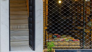 A building entrance with a staircase, a wooden planter with plants, and a chain-link fence with lights.
