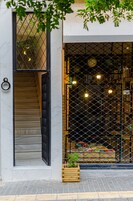 A building entrance with a staircase, a wooden planter with plants, and a chain-link fence with lights.
