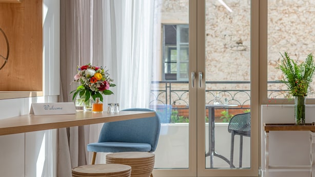 A modern hotel room with a wooden desk, a blue chair, and a balcony with a view of the outside.