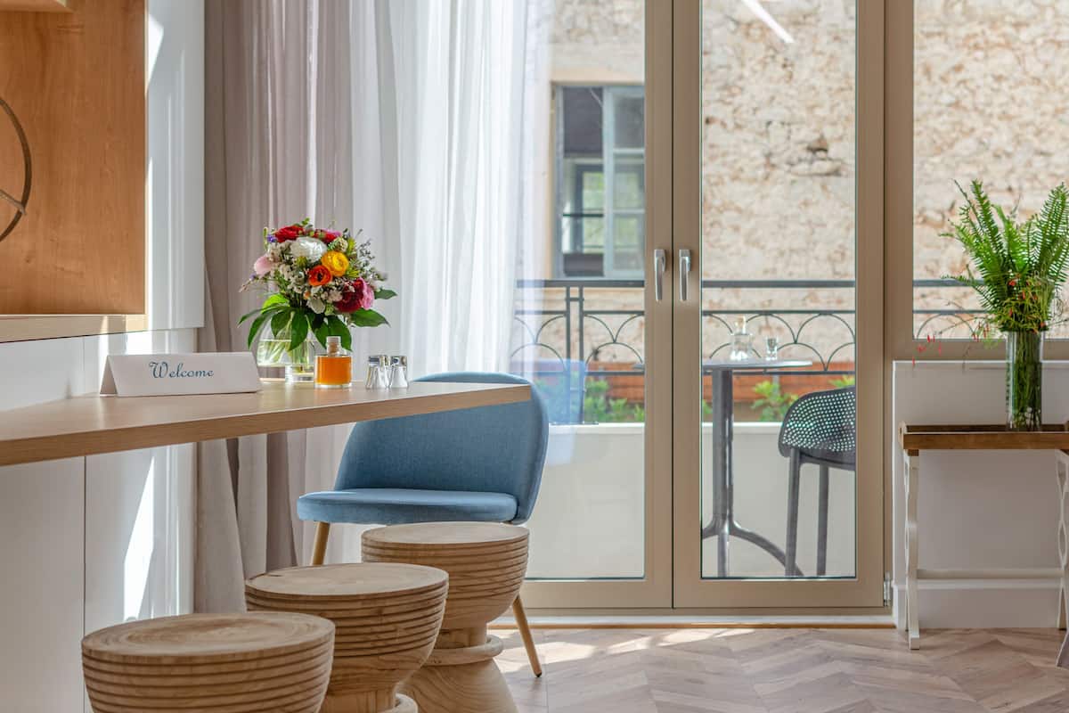Een moderne hotelkamer met een houten bureau, een blauwe stoel en een balkon met uitzicht.