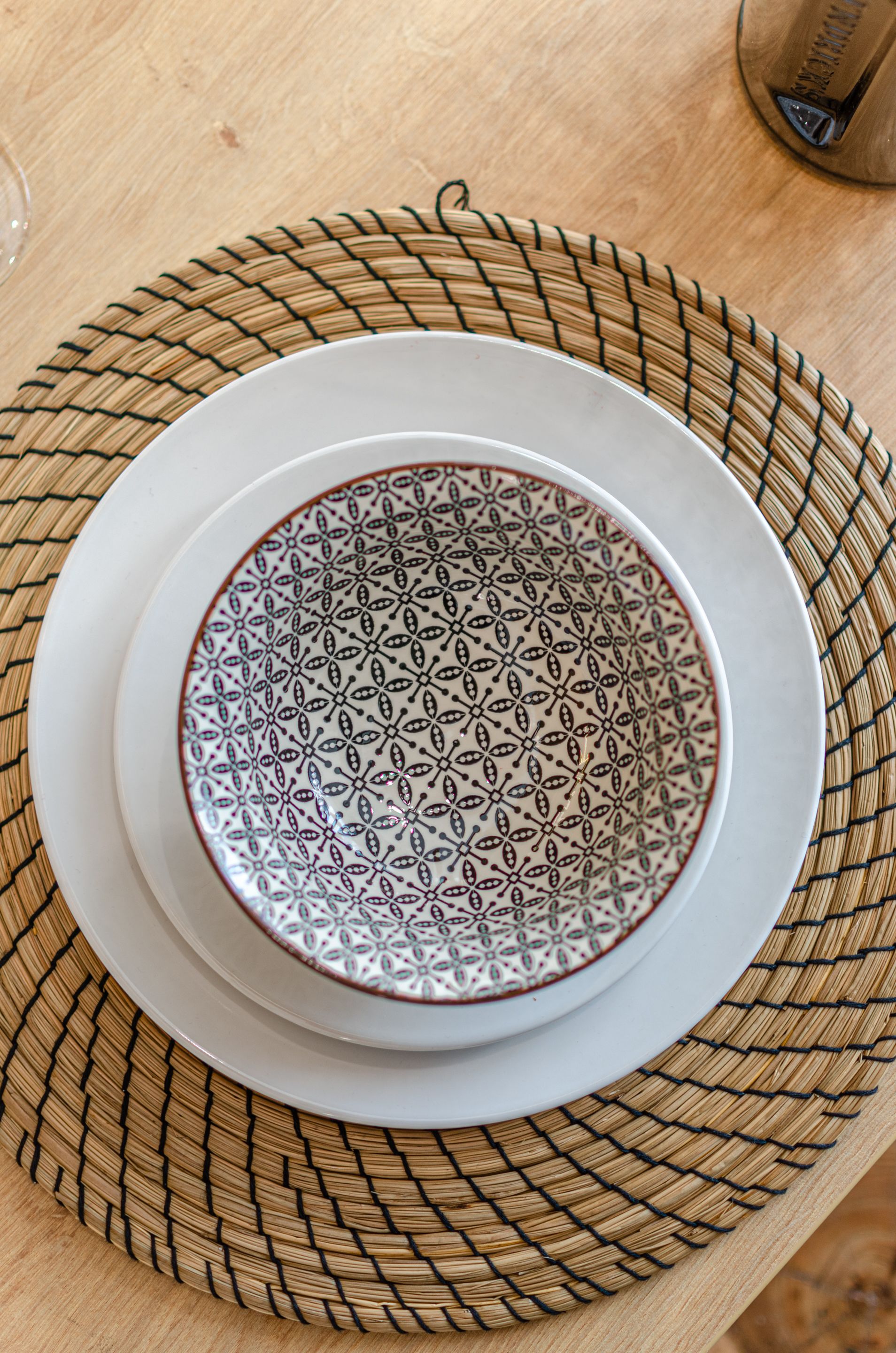 A table with a woven placemat, a white plate, and a patterned bowl.