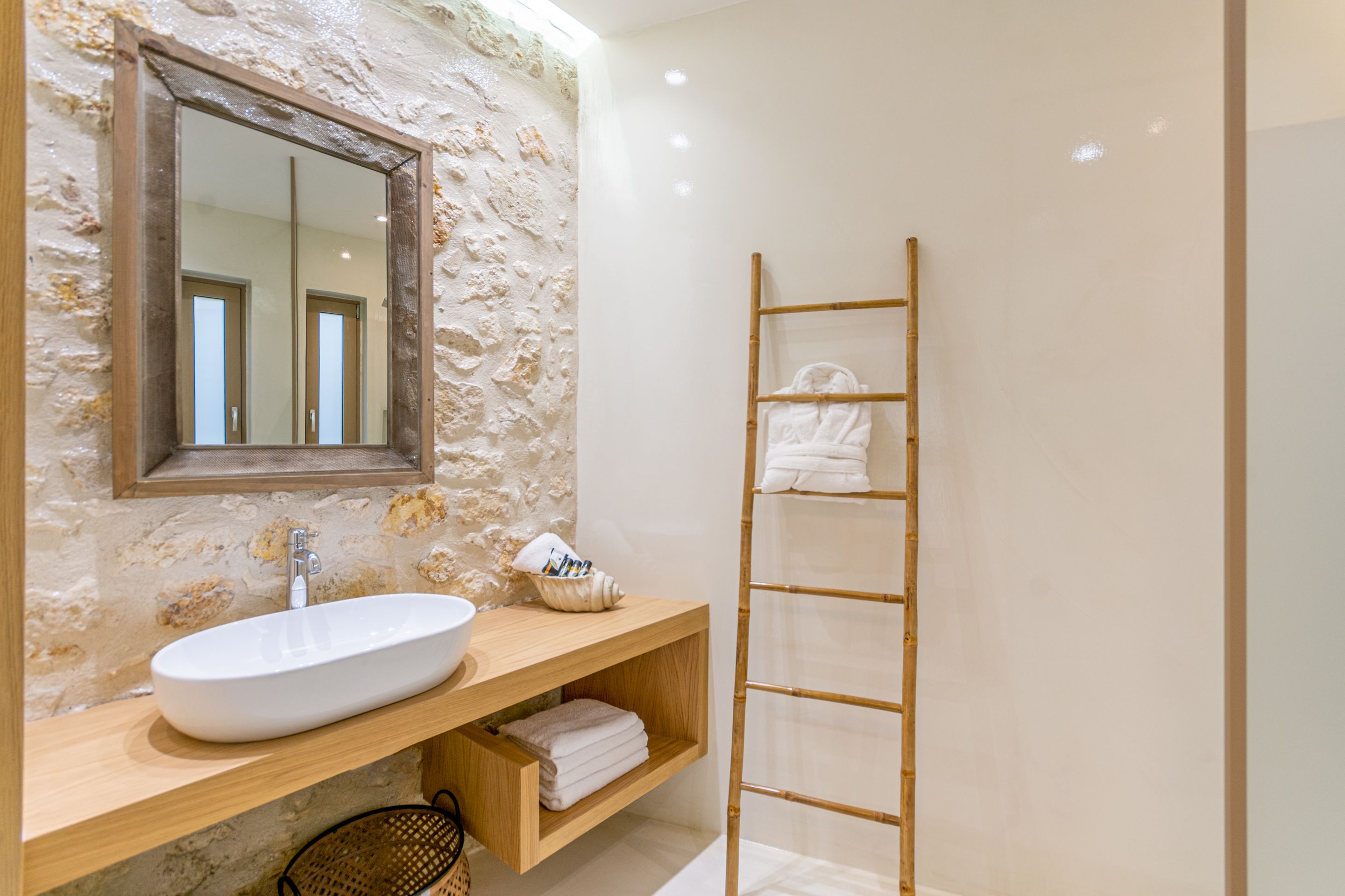 A bathroom with a stone wall, a wooden vanity, a white sink, a mirror, and a bamboo towel rack.