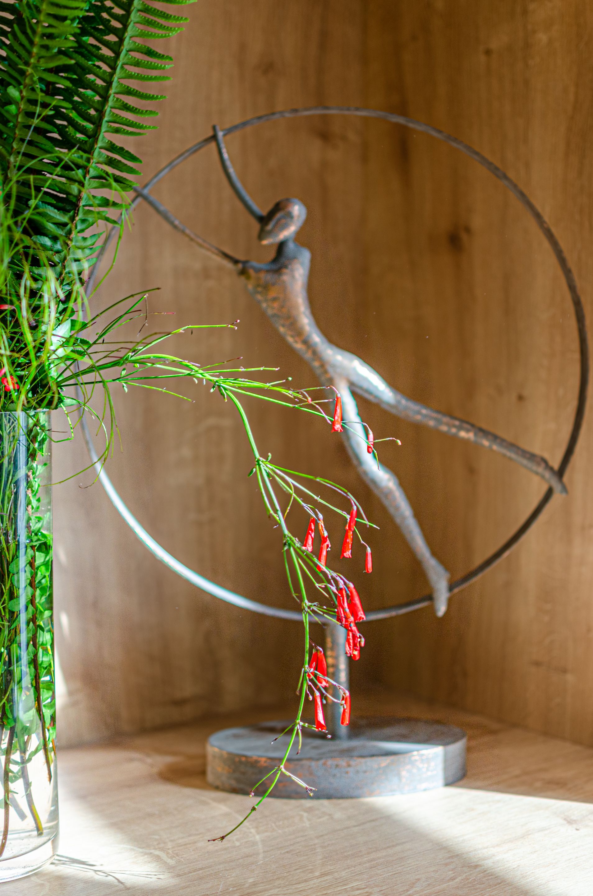 A sculpture of a lizard on a branch, placed on a circular base, with a potted plant to the left.