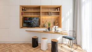 A modern living room with a wooden TV stand, a flat-screen TV, a dining table, and a chair.