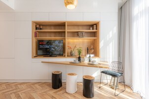 A modern living room with a wooden TV stand, a flat-screen TV, a dining table, and a chair.