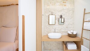 A bathroom with a stone wall, a wooden vanity, a white sink, and a towel rack.